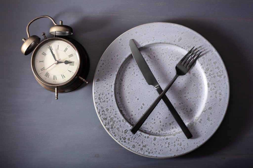 concept intermittent fasting, ketogenic diet, weight loss. fork and knife crossed plate alarmclock